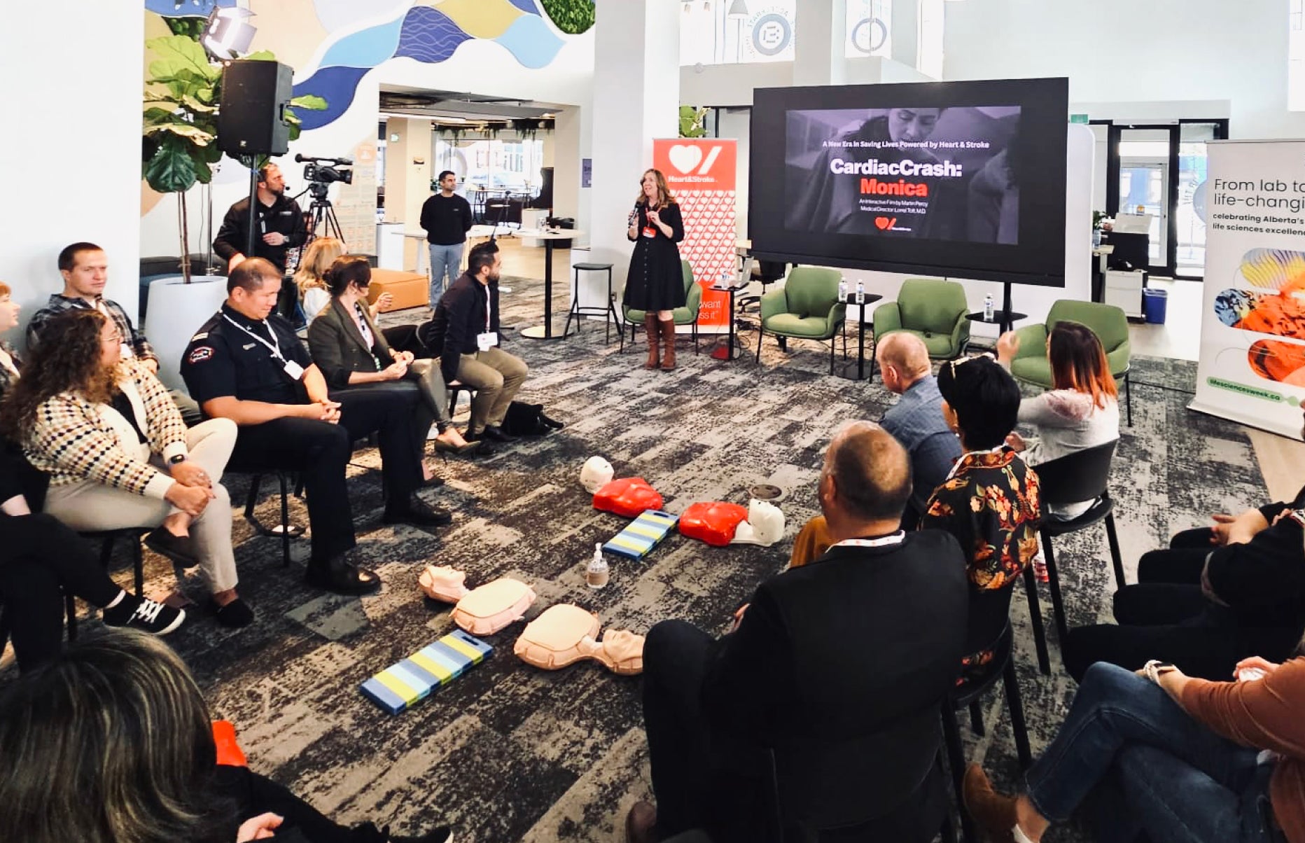 A woman in her 40s facilitating a CardiacCrash course to a group of 20 employees in an office setting