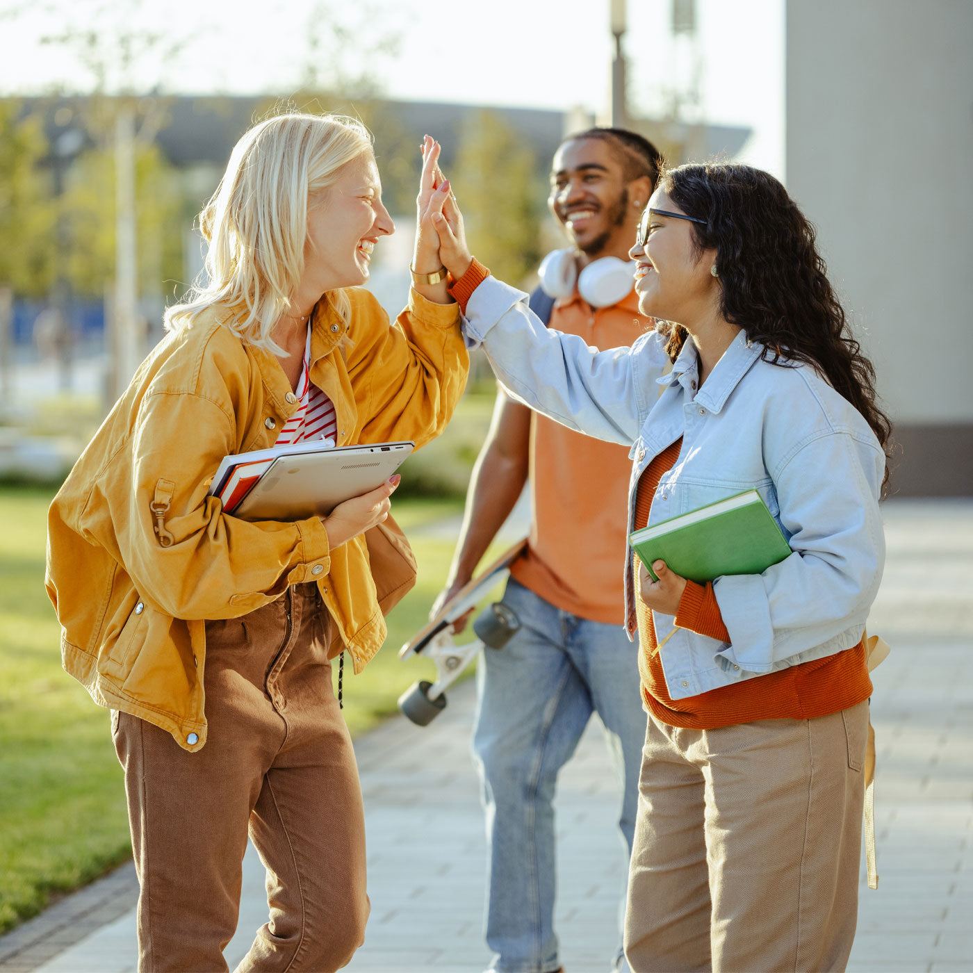 3 smiling high school students walking outside to class, 2 girls are high fiving each other