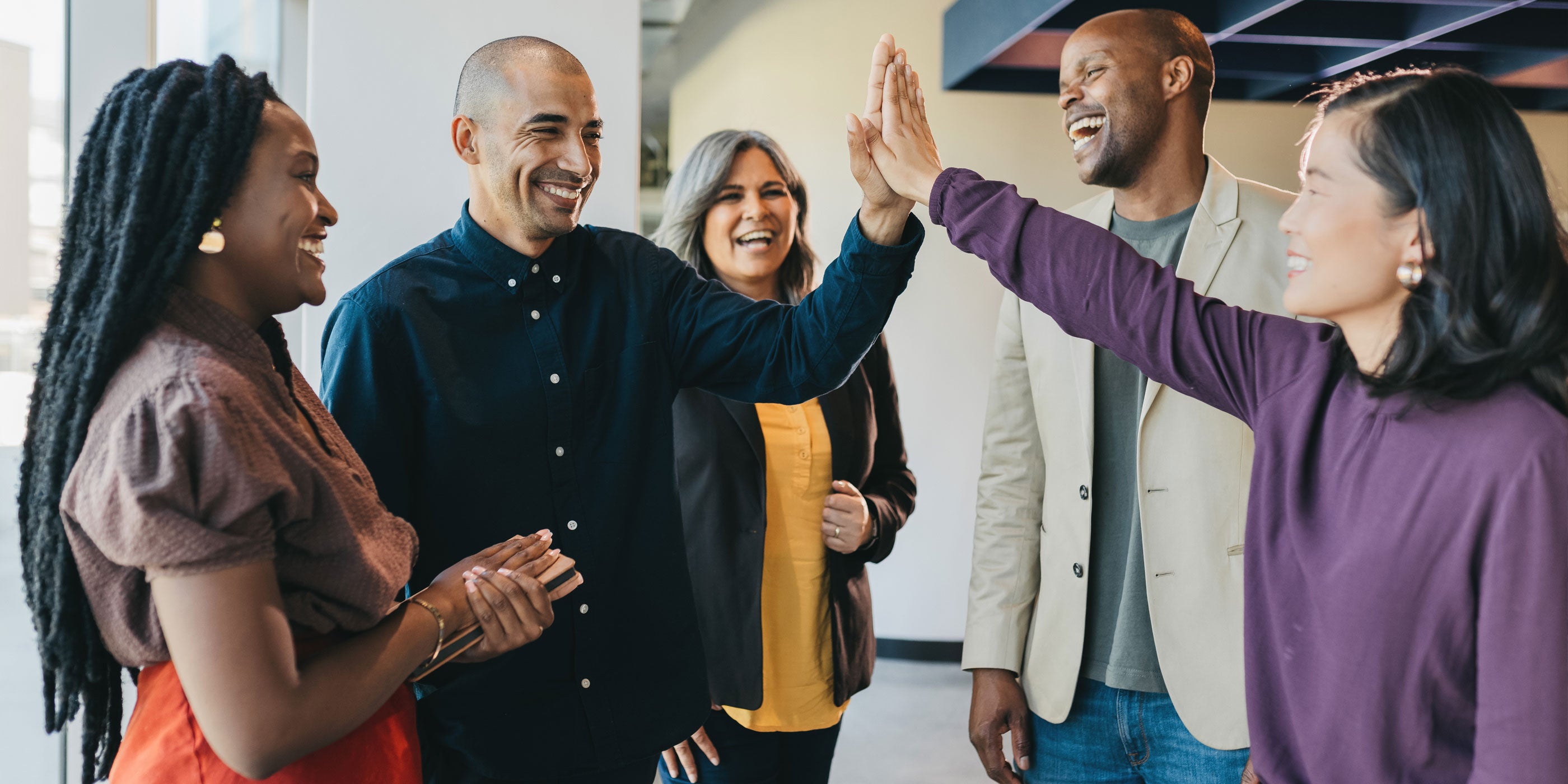 A multicultural group of smiling adults, 2 are high fiving each other