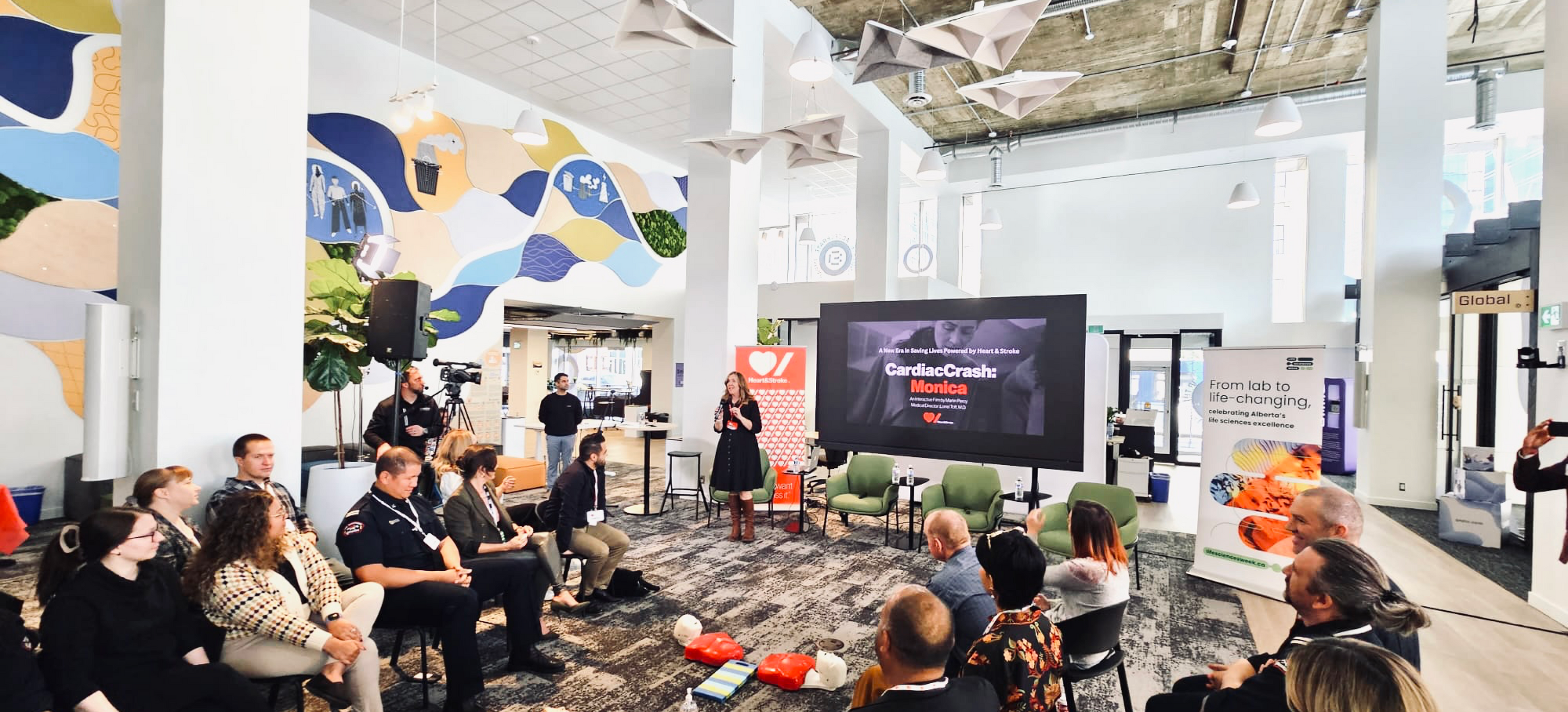 A woman in her 40s facilitating a CardiacCrash course to a group of 20 employees in an office setting