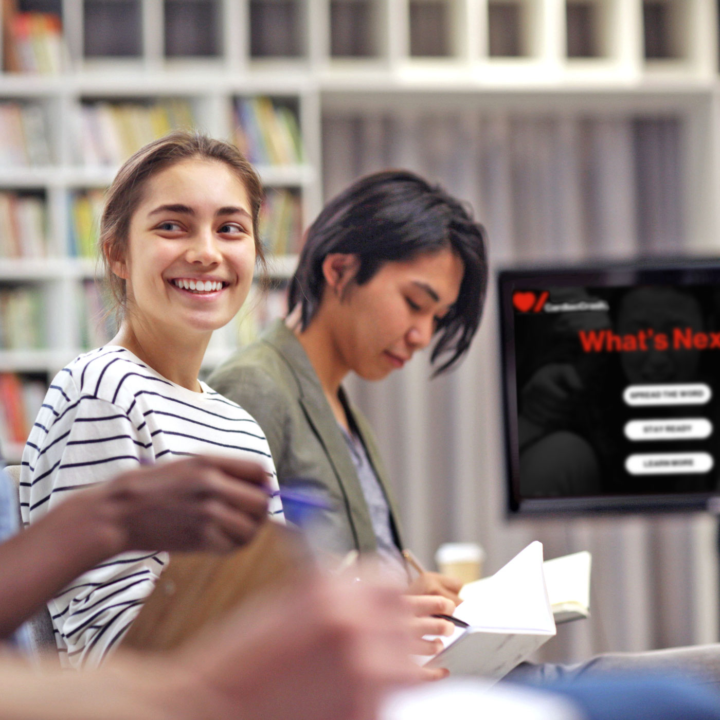 Two smiling female students taking notes in a classroom during a CardiacCrash course