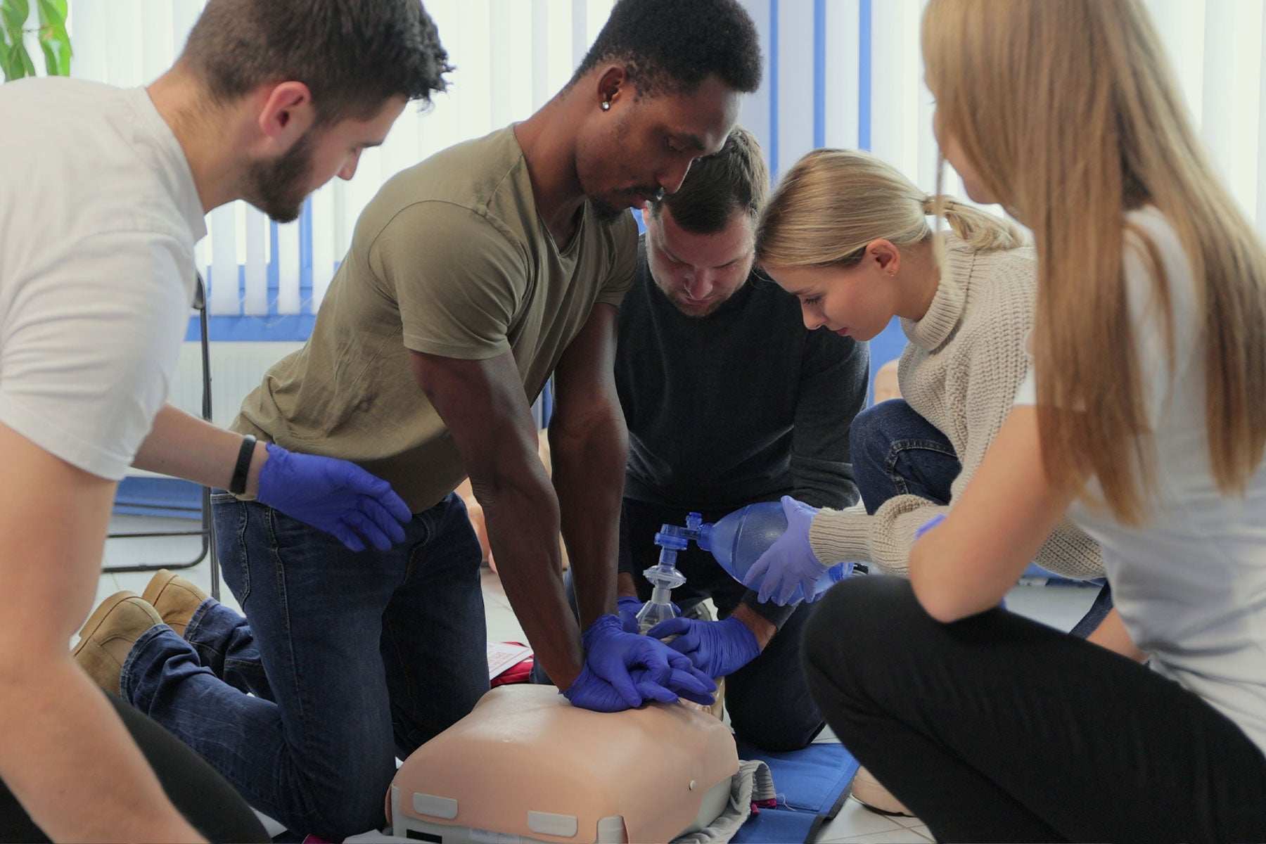 A group of 5 adults performing CPR on a training dummy