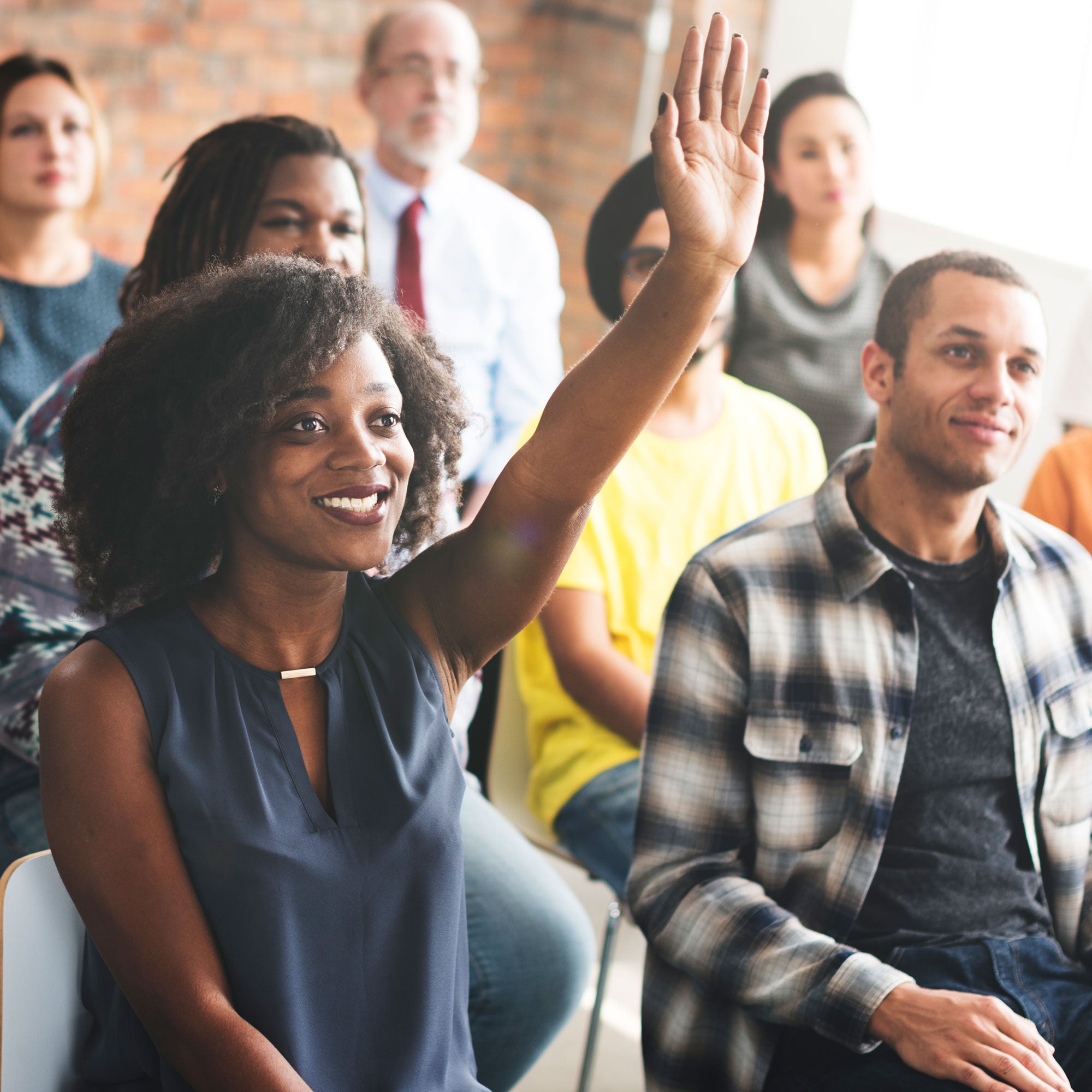 A smiling woman raising her hand in a classroom full of adult students