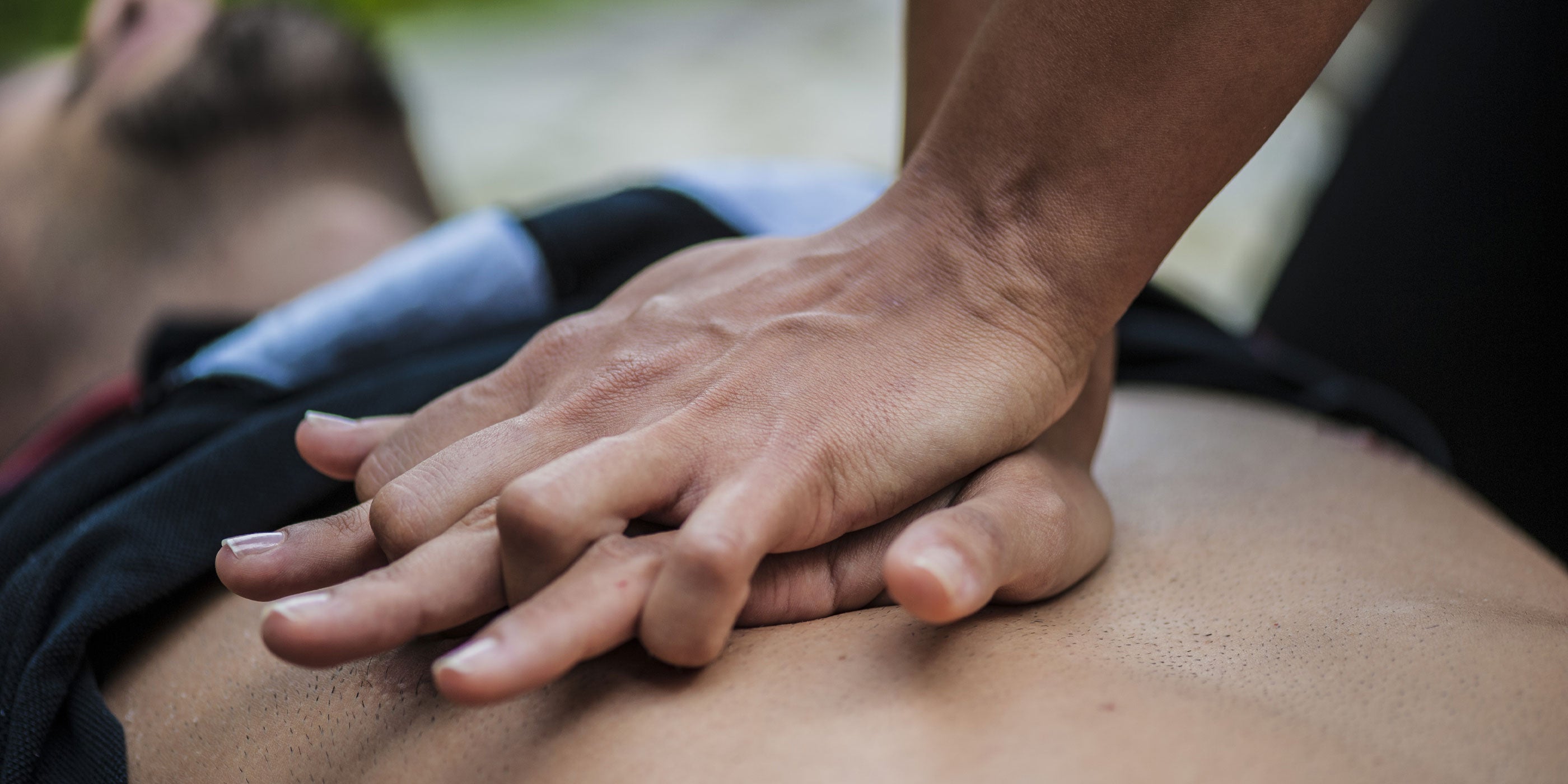 A close up of a woman's hands performing CPR on a man's chest