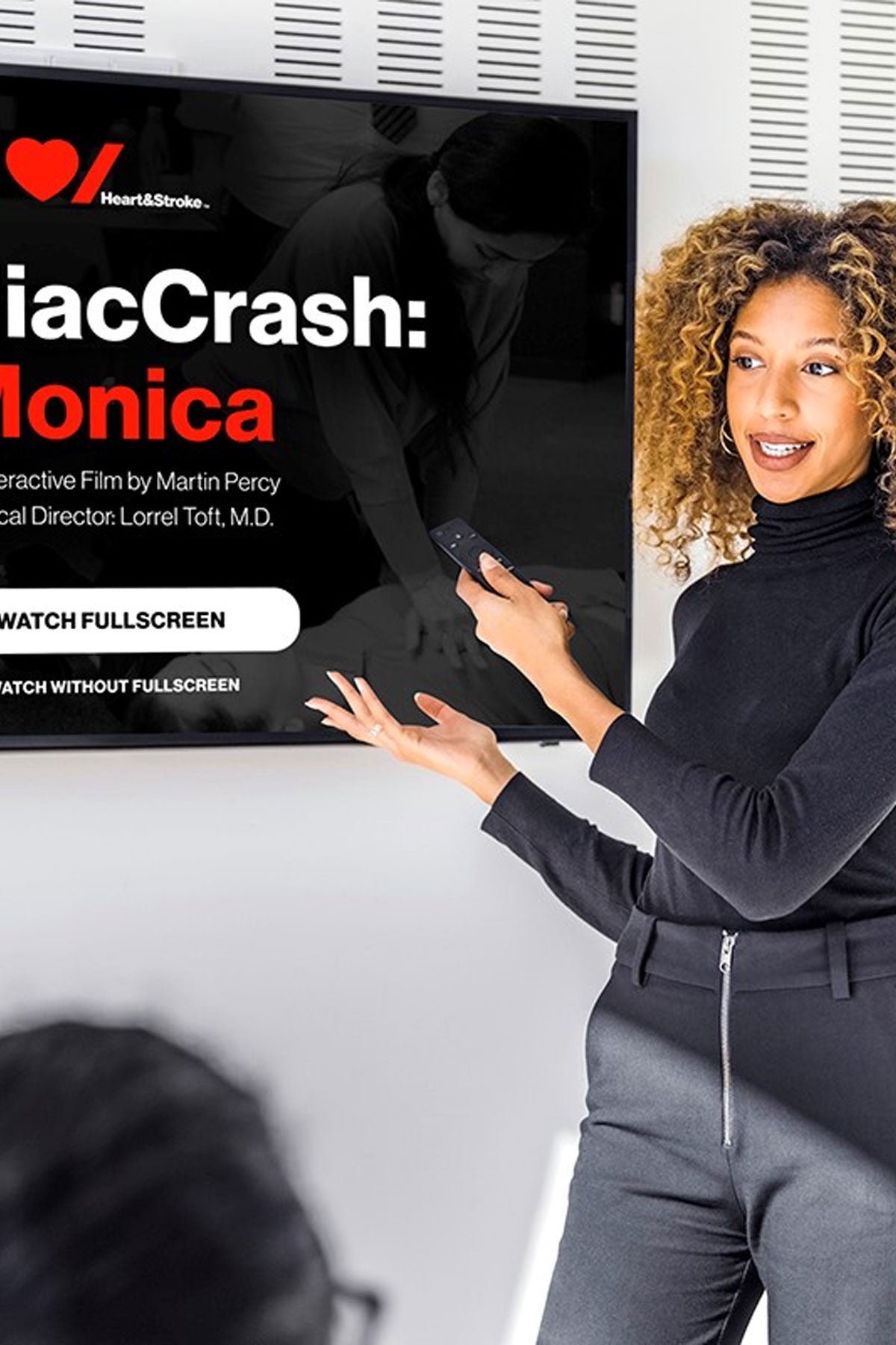 A woman in her 30s beside a TV ready to play a CardiacCrash video