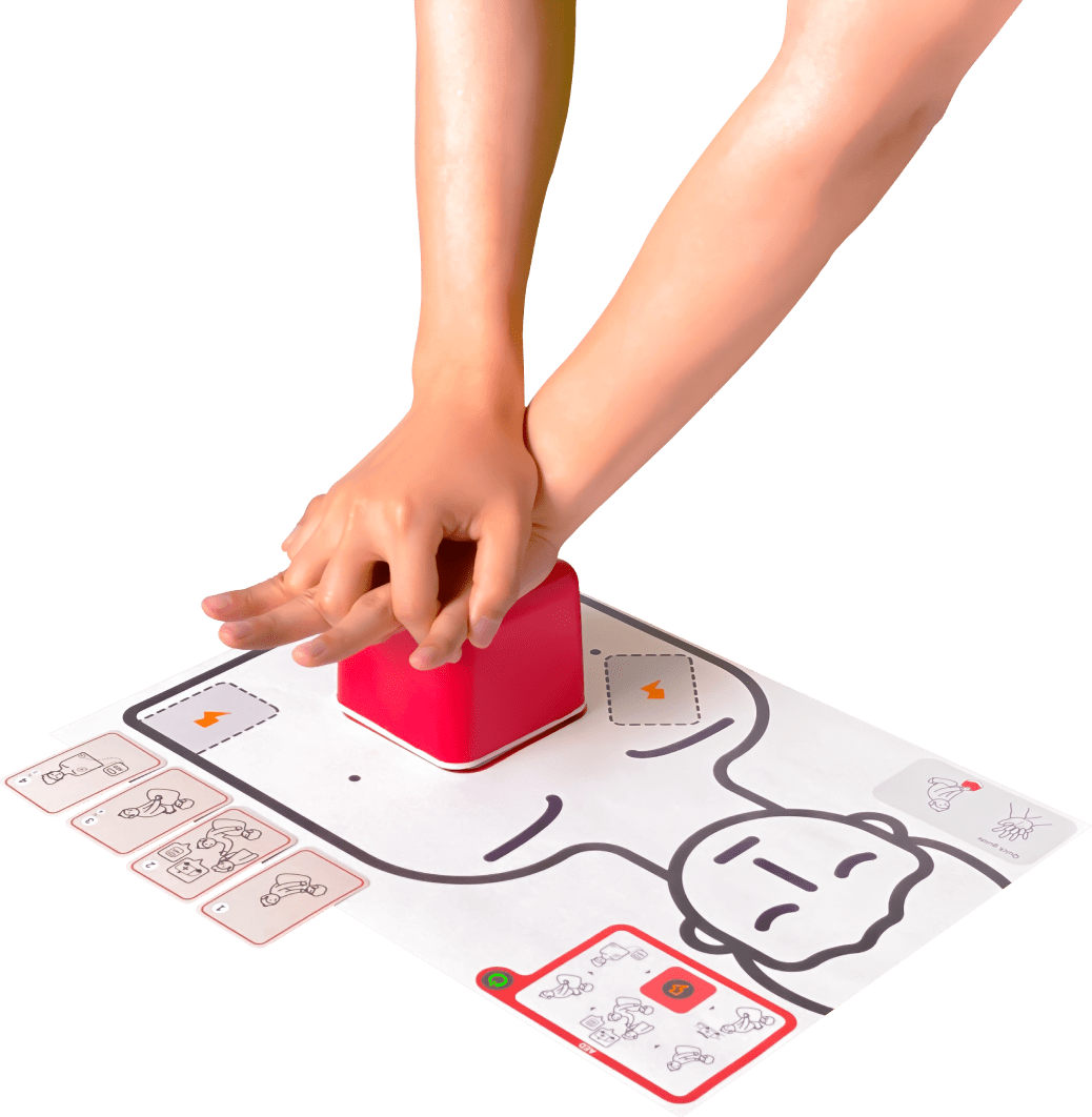2 hands performing CPR on a red cube that is sitting on a paper graphic of someone's chest